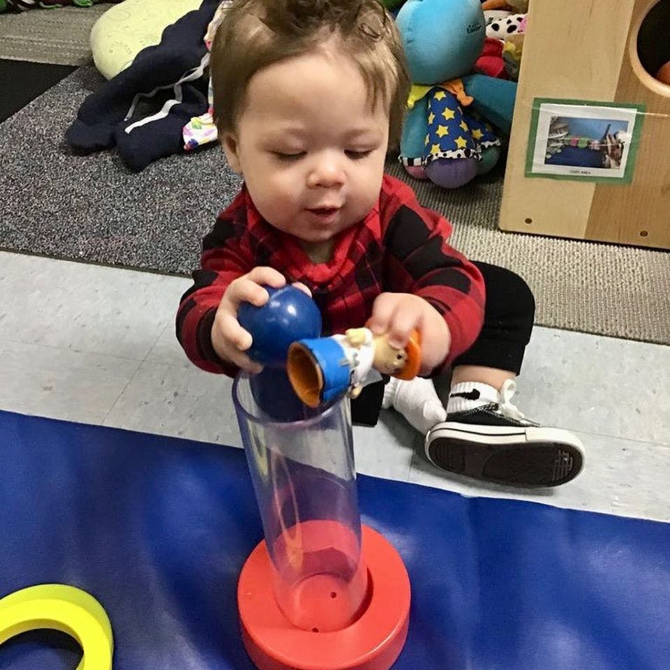 Child playing with a blue ball and a toy figure over a clear tube