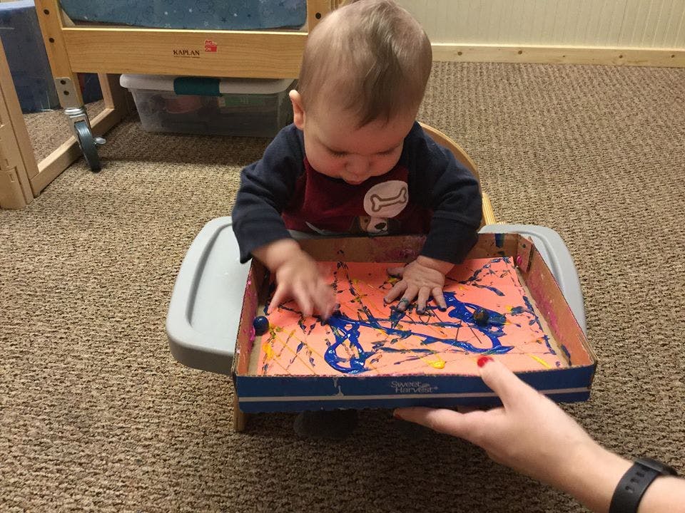 Child in high chair playing with paint in a box