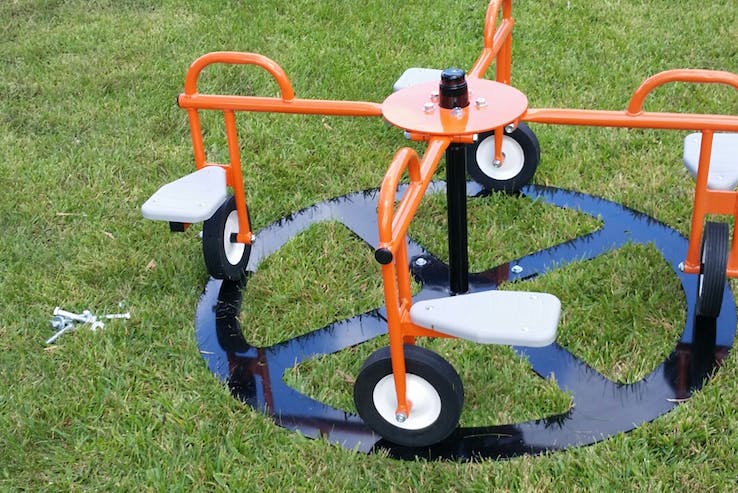 Orange playground merry-go-round with seats and wheels on grass