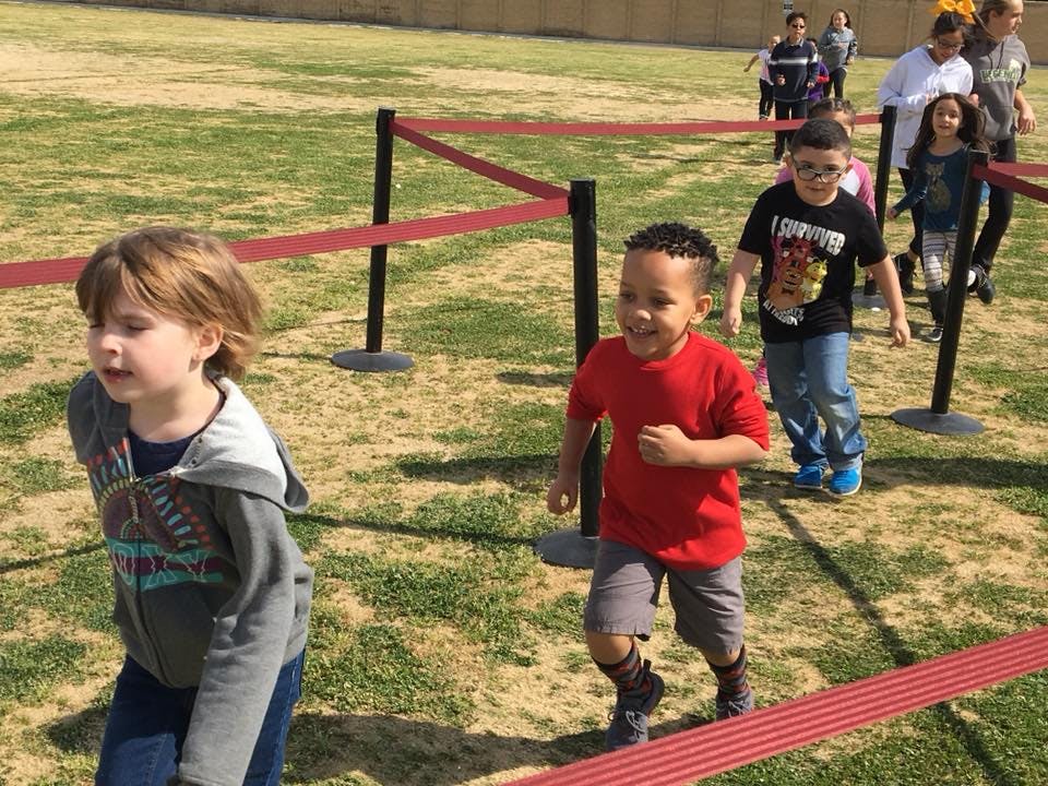 Children running on a grassy field between red ropes