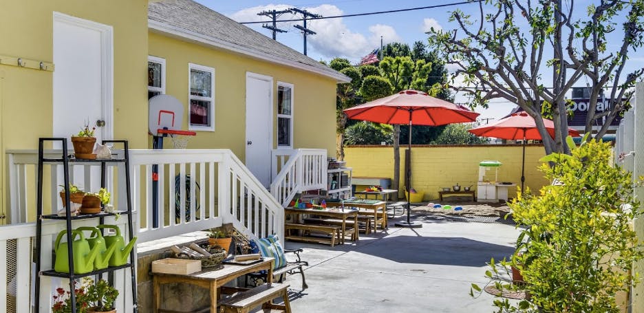 Backyard with yellow house, white stairs, and red umbrellas