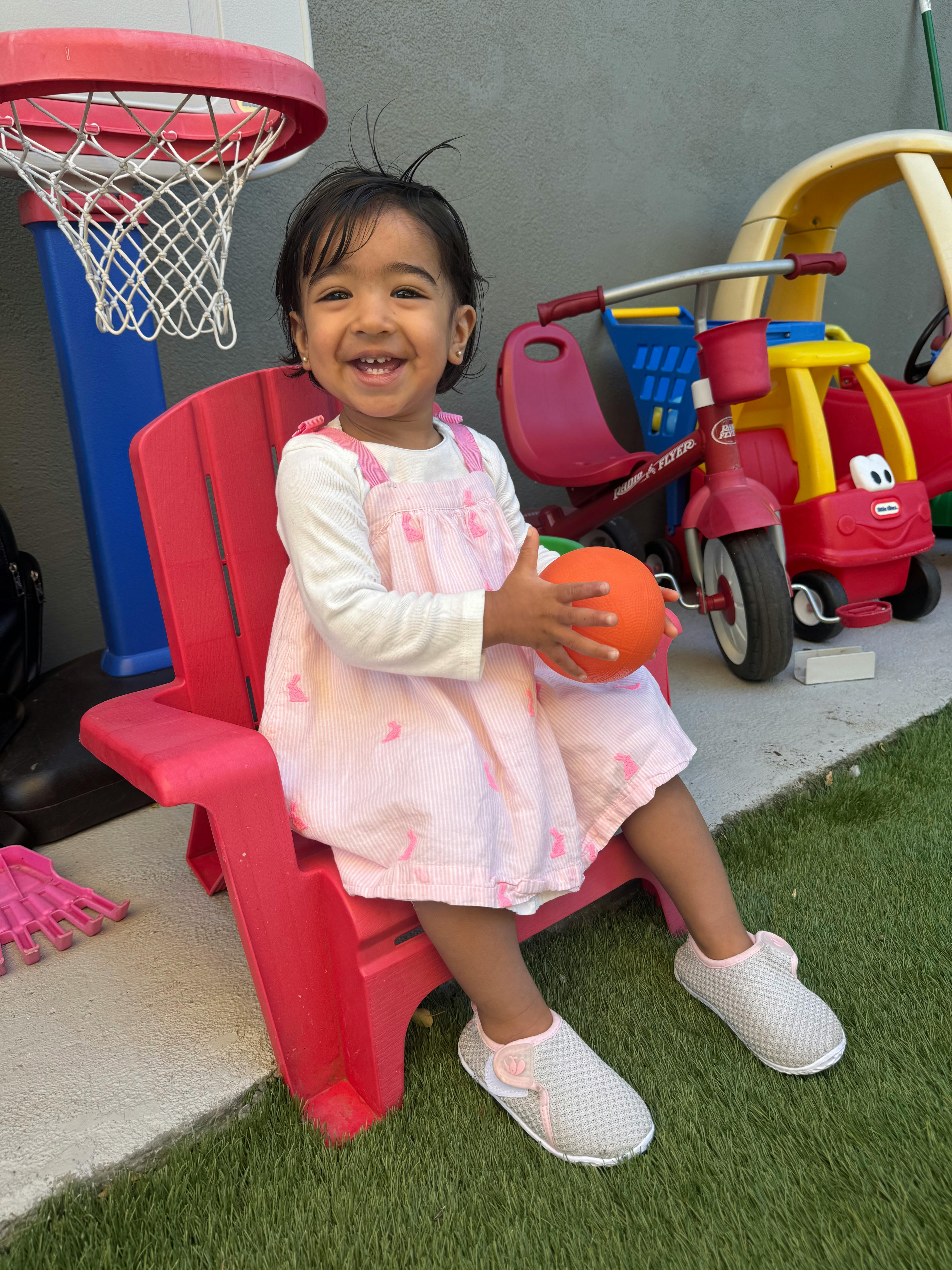 Child sitting in a red chair holding a small orange ball