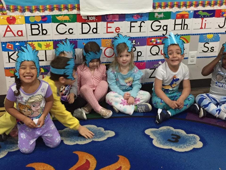 Children wearing blue paper crowns sitting on a rug in a classroom