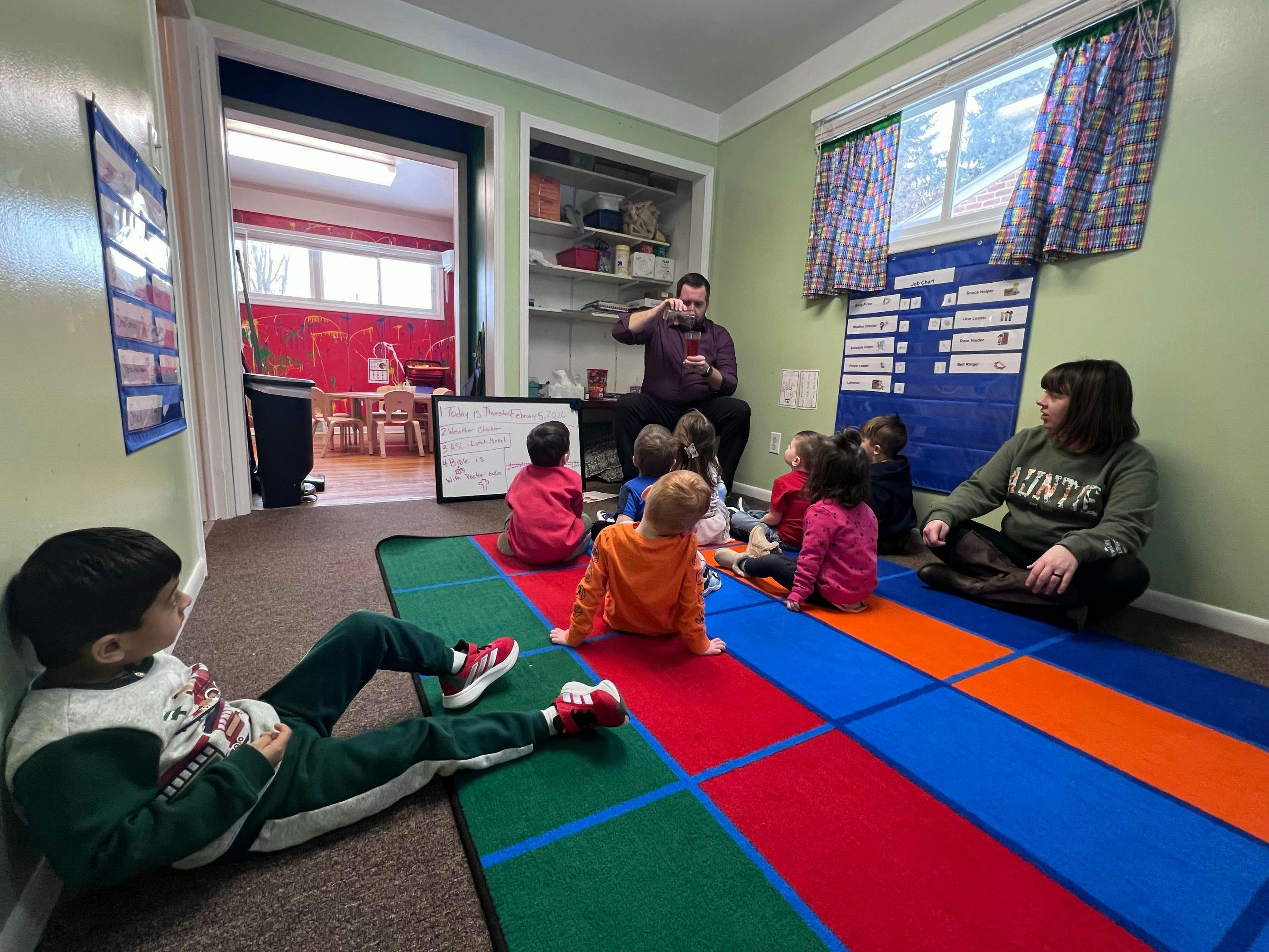A person pouring liquid into a glass in front of children in a classroom