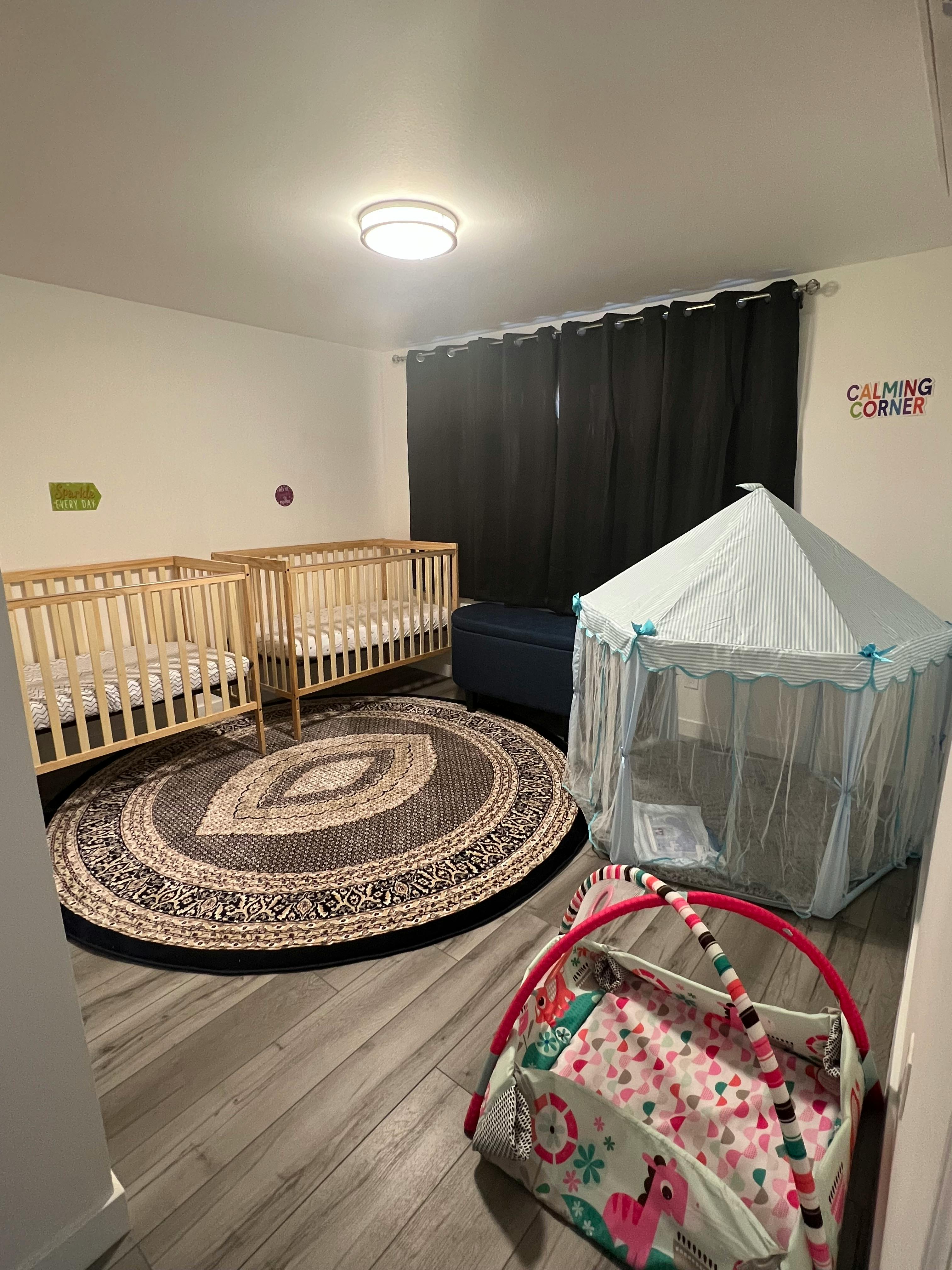 Two cribs, a play tent, and a round rug in a room