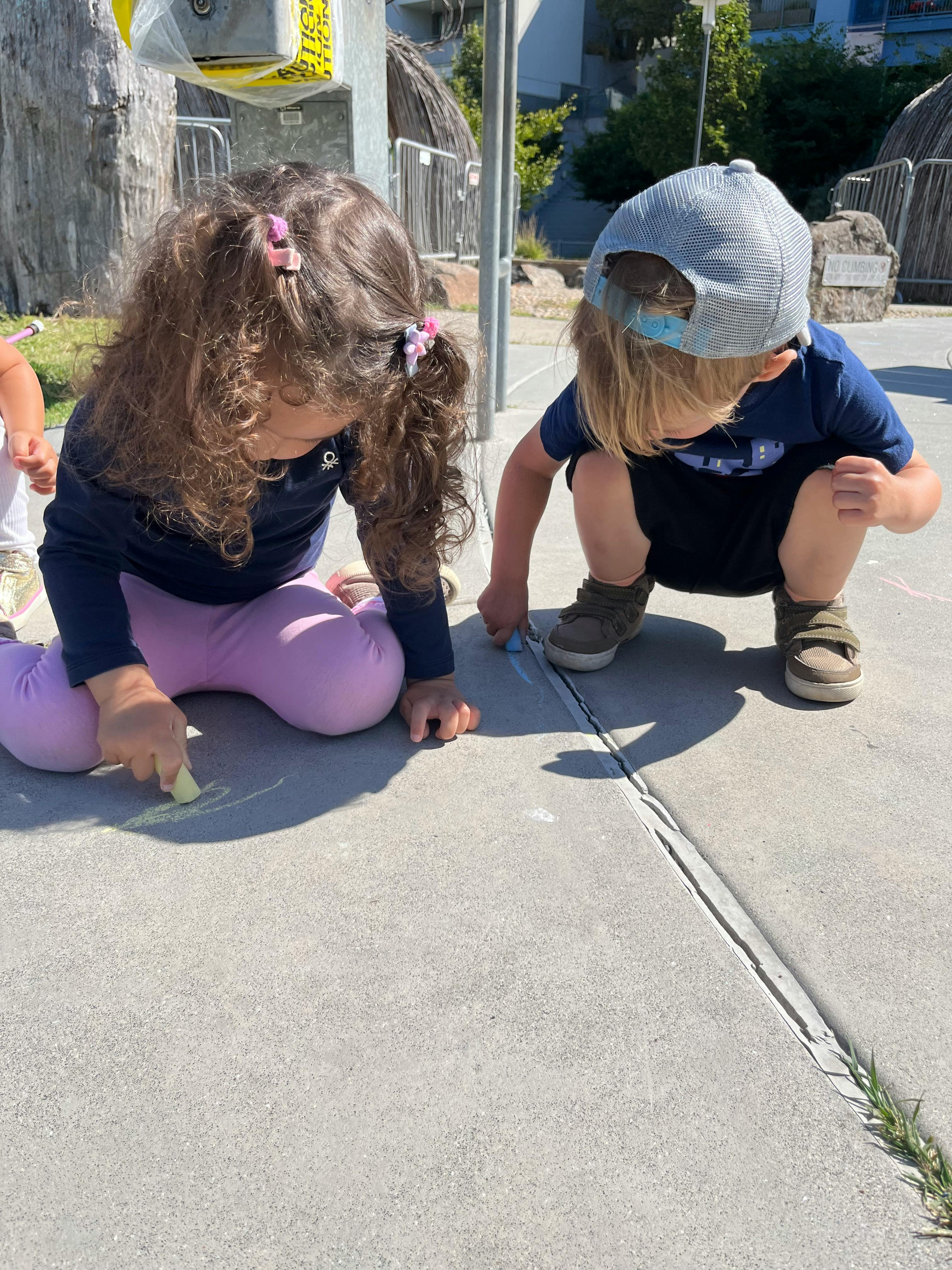 Two children drawing with chalk on pavement