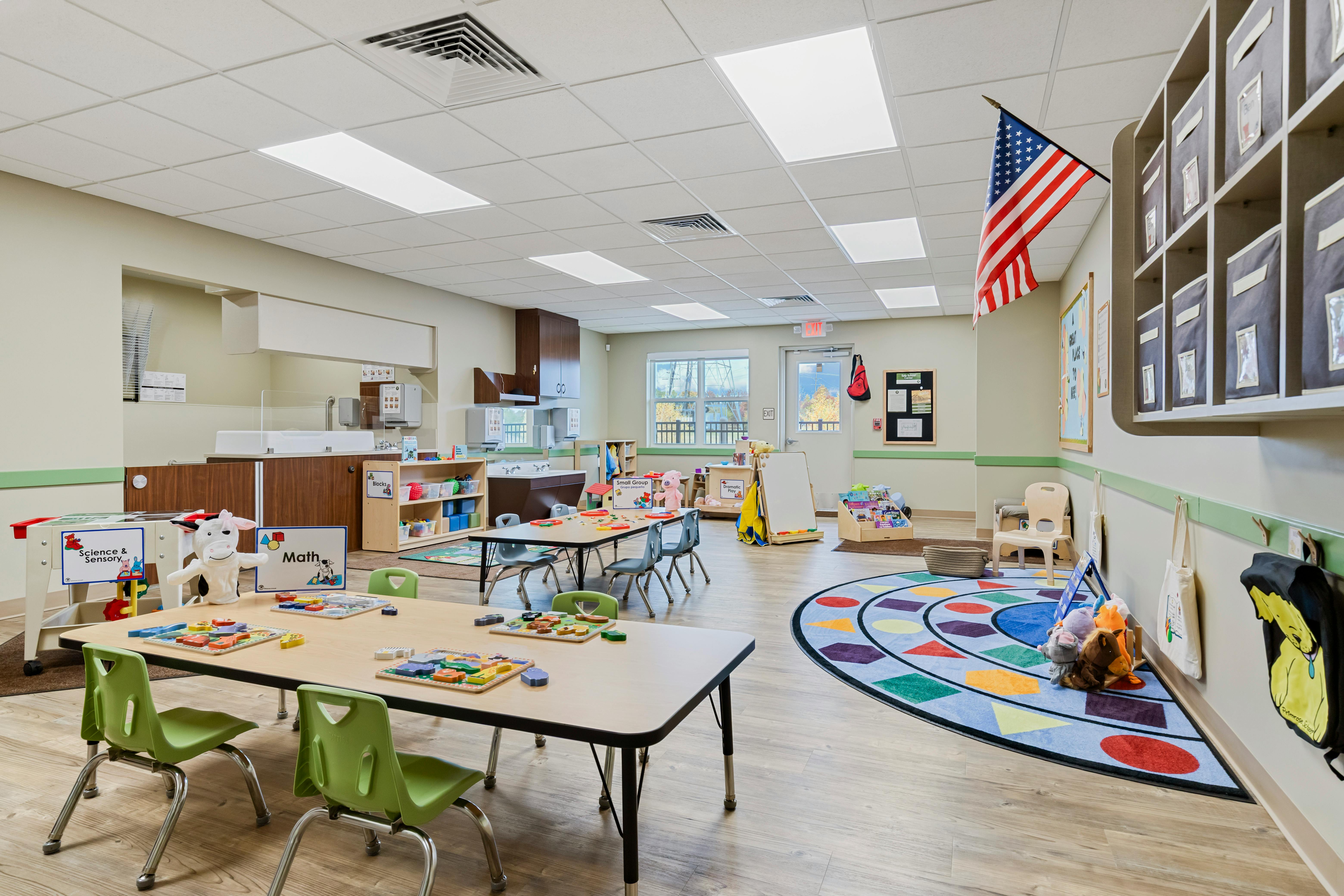 Classroom with tables, chairs, shelving units, and a colorful circular rug
