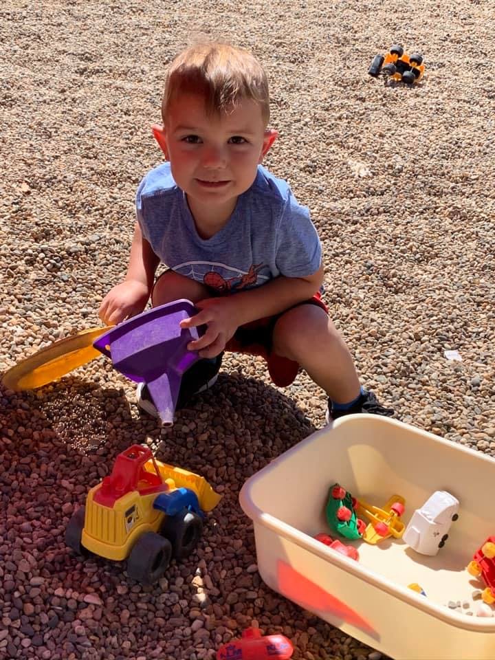 Child playing with a purple funnel and toy truck in gravel