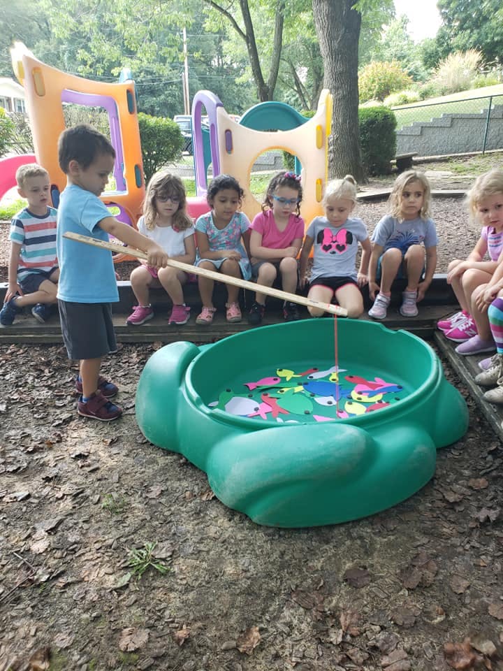 Child fishing in a turtle-shaped sandbox with other children watching