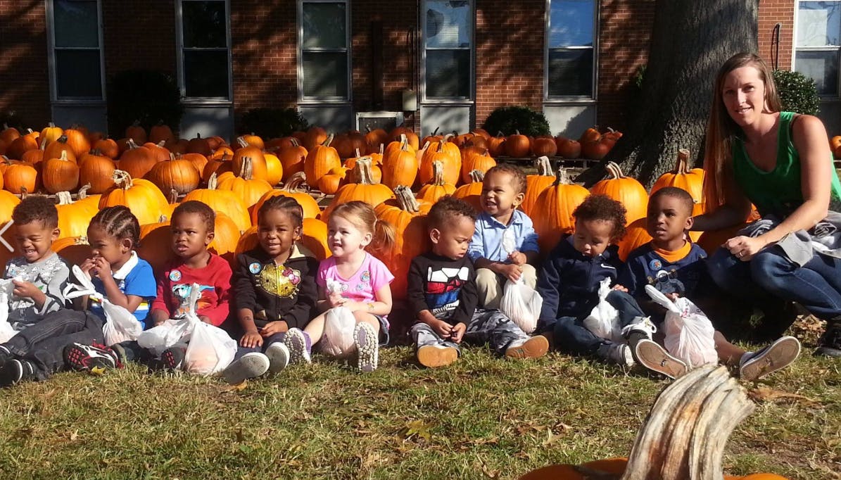 Adult and children sitting in front of pumpkins