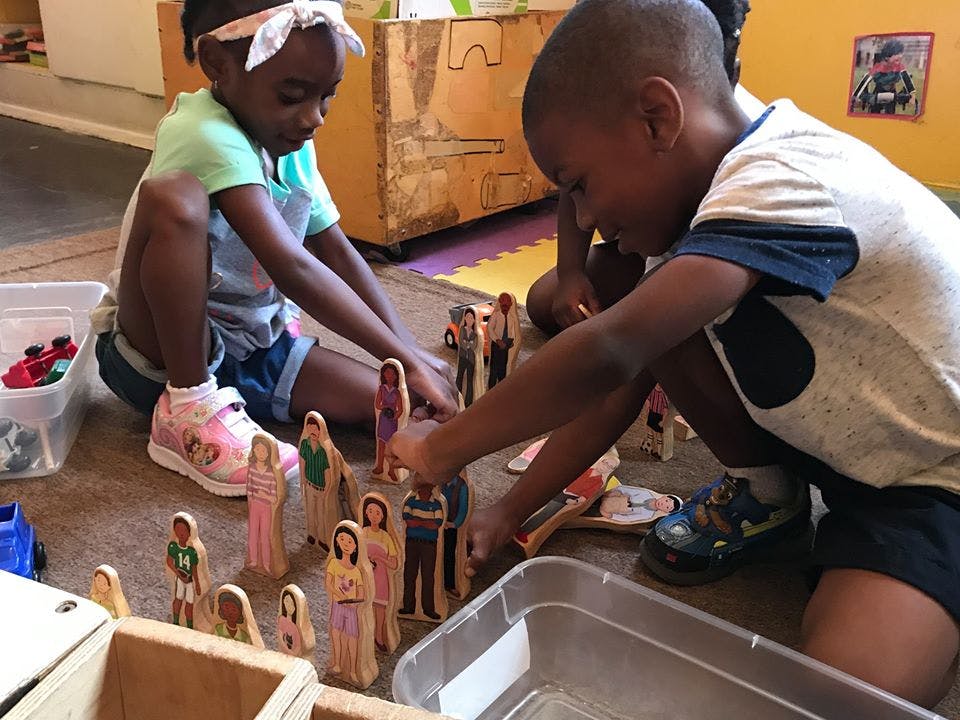 Two children playing with wooden figures on the floor