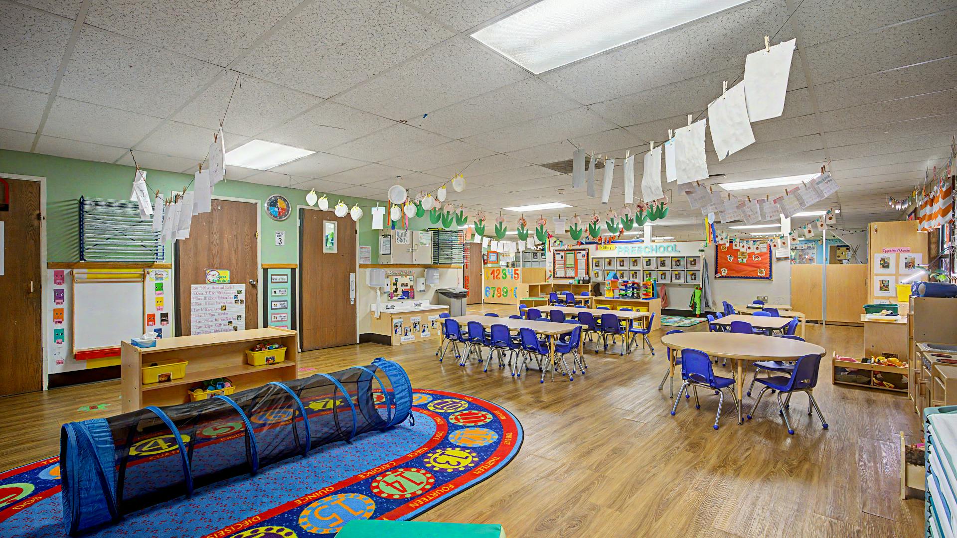 Classroom with tables, chairs, and play tunnel on a colorful rug