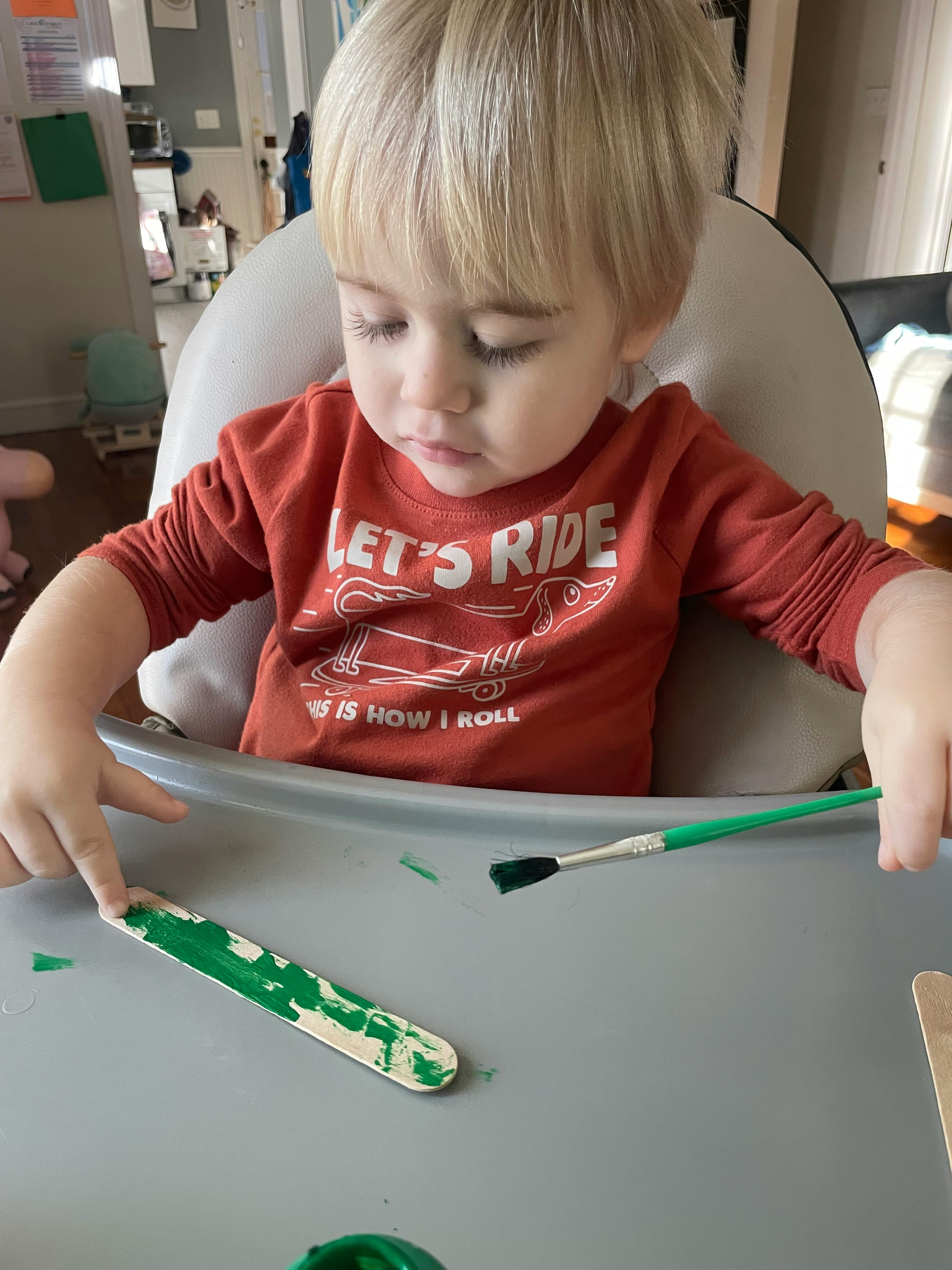 Child painting a craft stick green with green paint