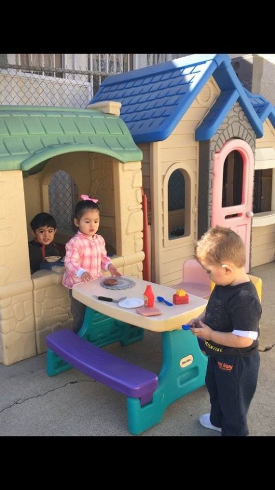 Three children playing with a toy picnic table and playhouses