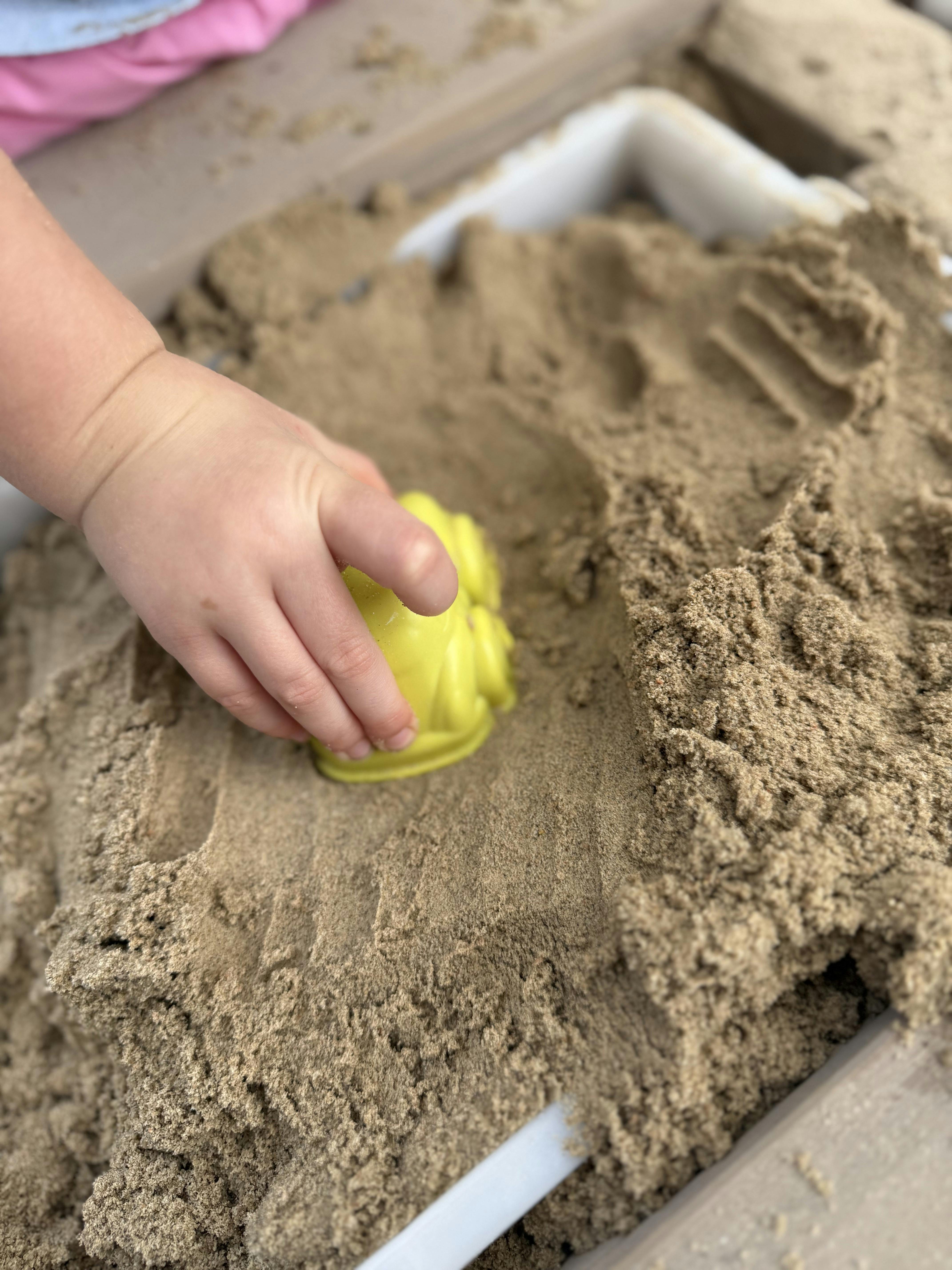 Child hand pressing a yellow toy into kinetic sand