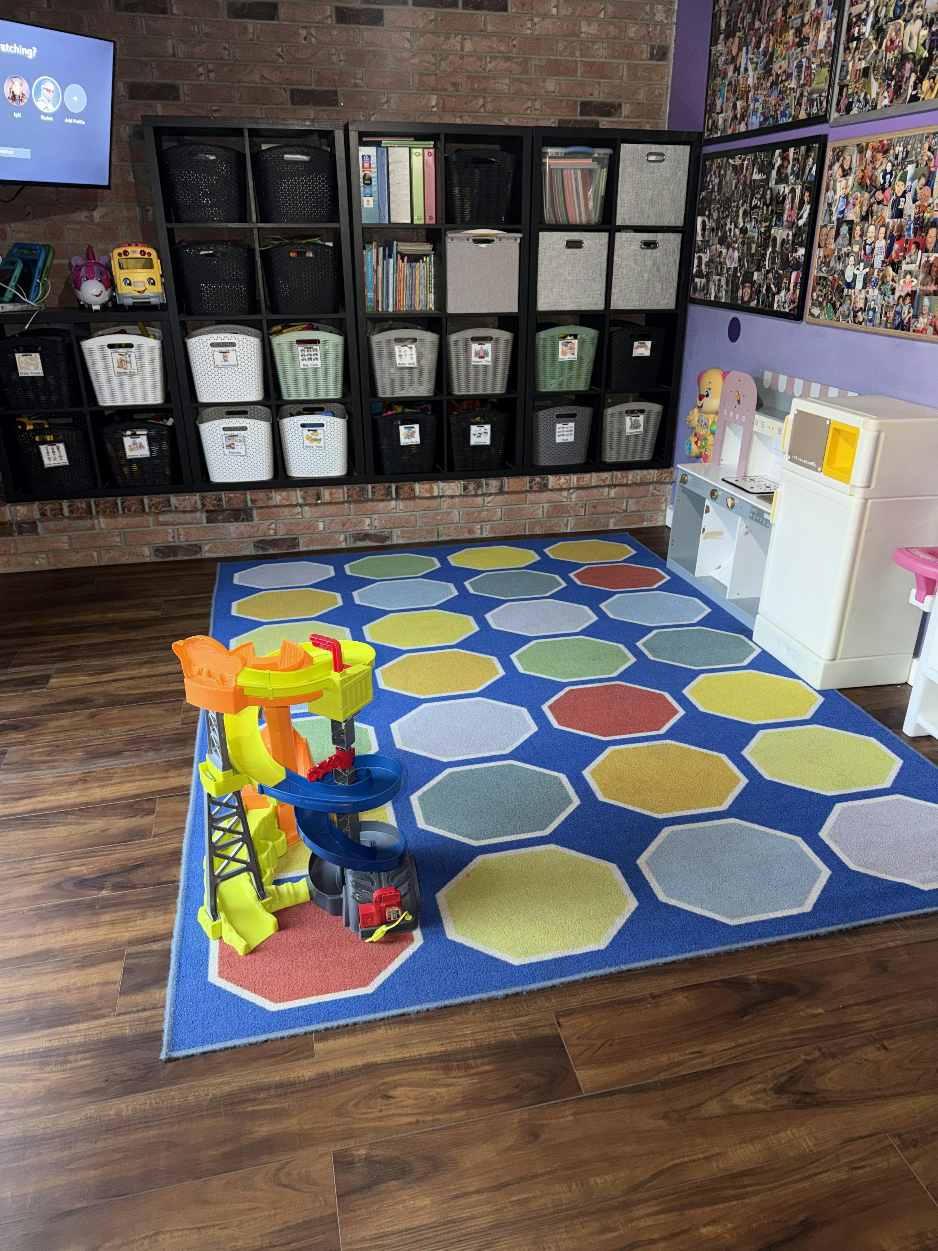 A colorful play rug with a toy car garage, shelves of storage bins, and toy kitchen