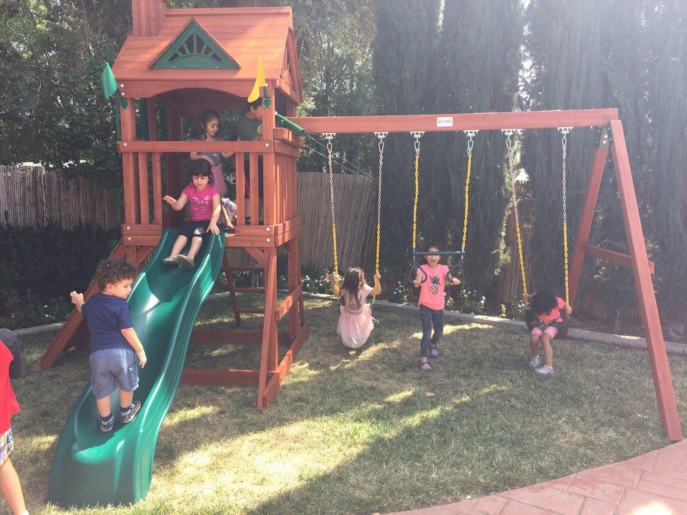 Children playing on a wooden playset with a slide and swings