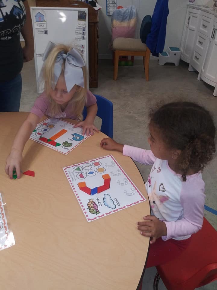 Two children at a table playing with learning materials
