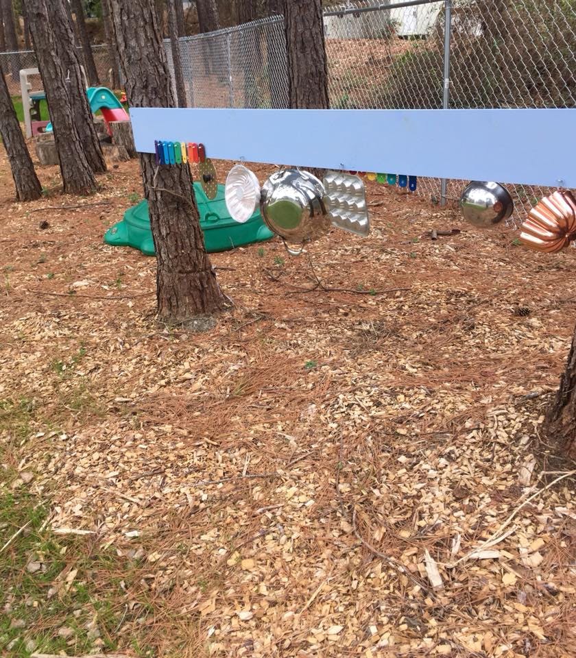 Outdoor play area with metal objects hanging from a blue board between trees