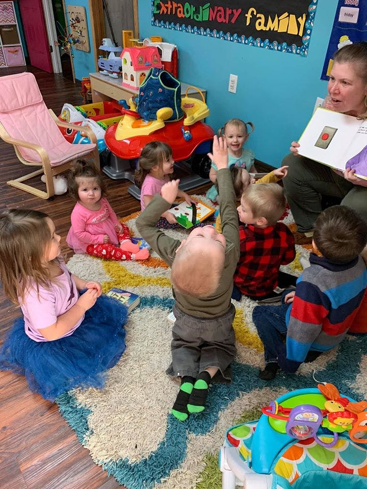 Adult reading a book to a group of children sitting on a rug