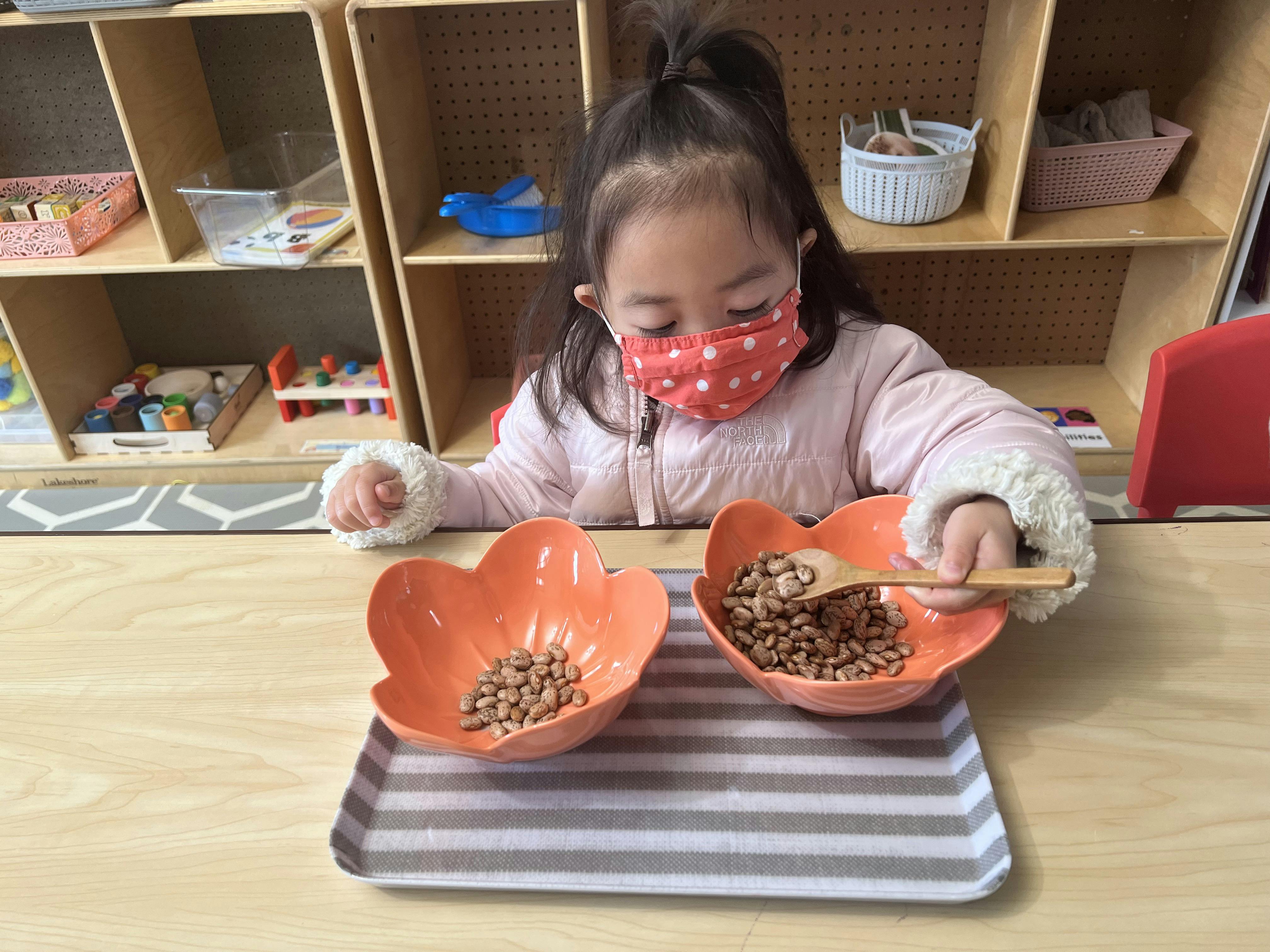 Child in a mask scooping beads from one bowl to another