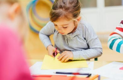 Child cutting yellow paper with scissors