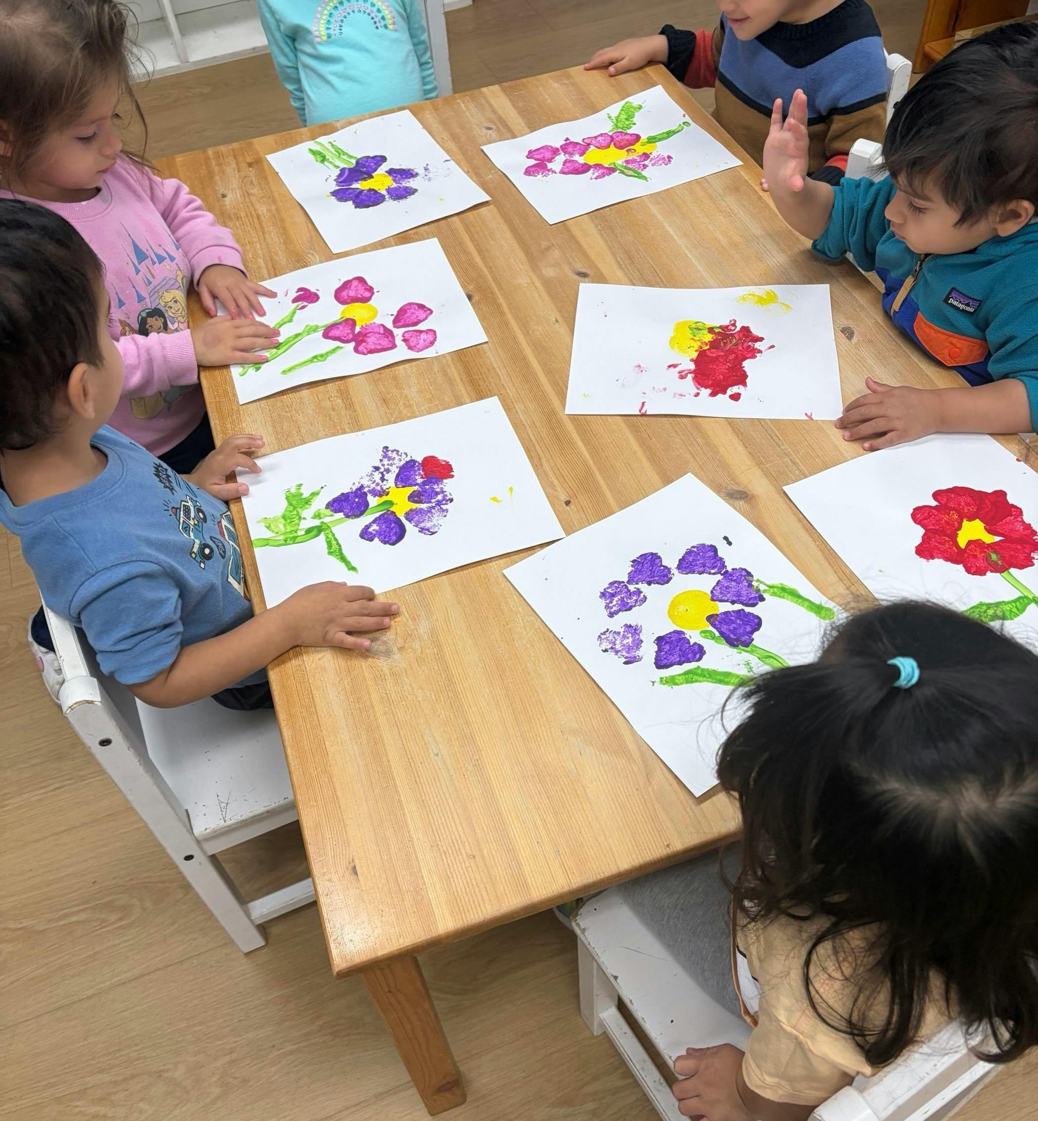 Children sitting at a table with their flower paintings