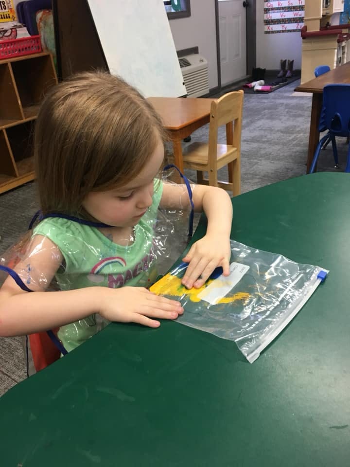 Child in a classroom painting inside a plastic bag
