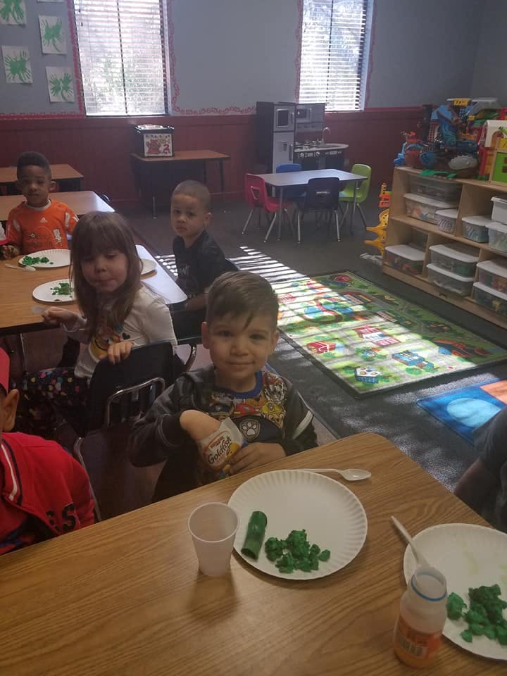 Children sitting at tables in a classroom with green playdough