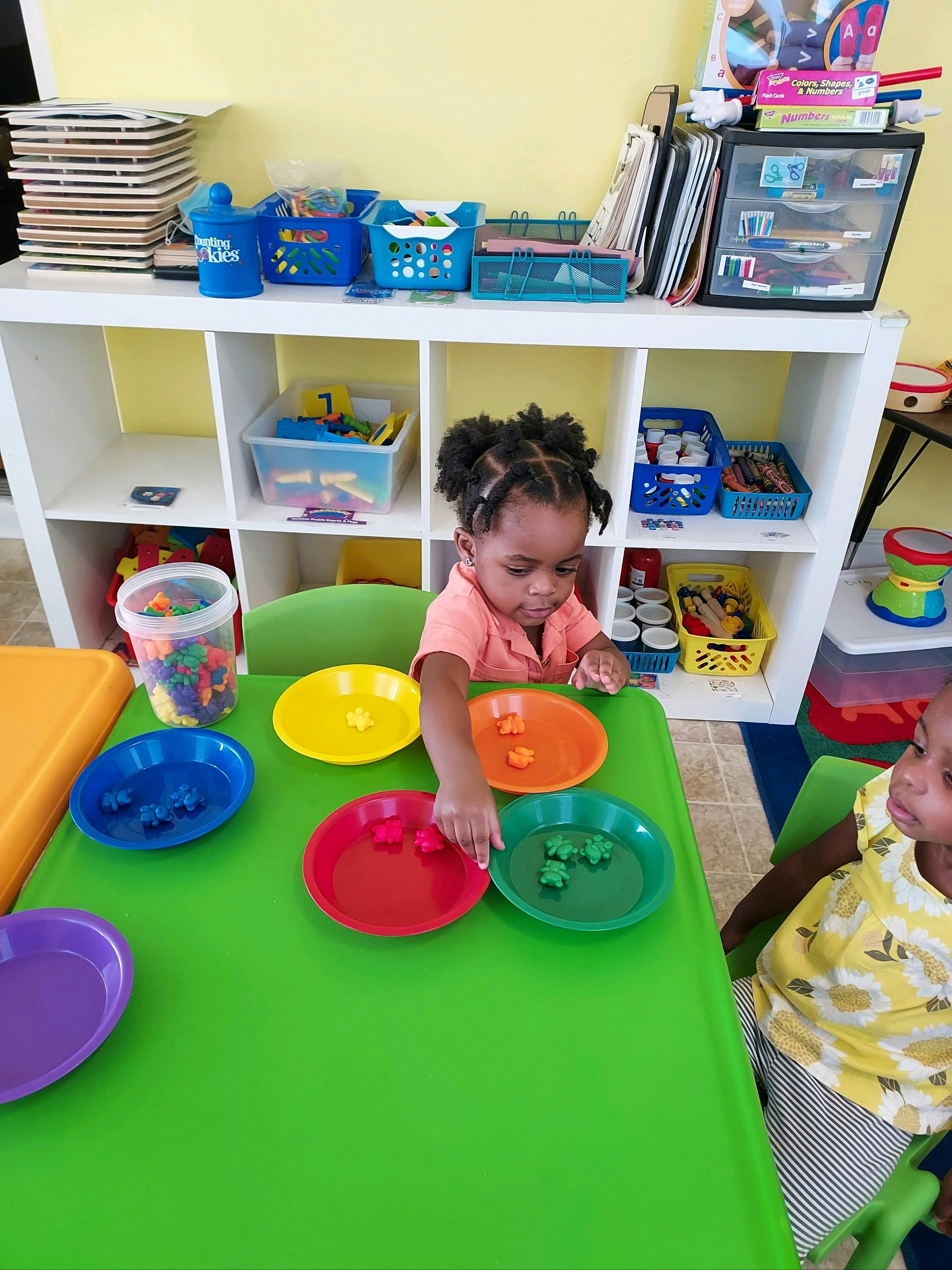 Child sorting small objects into colored plates at a table