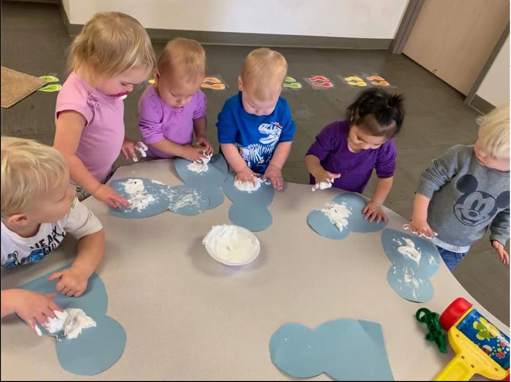 Children doing an art activity with shaving cream on blue paper cutouts