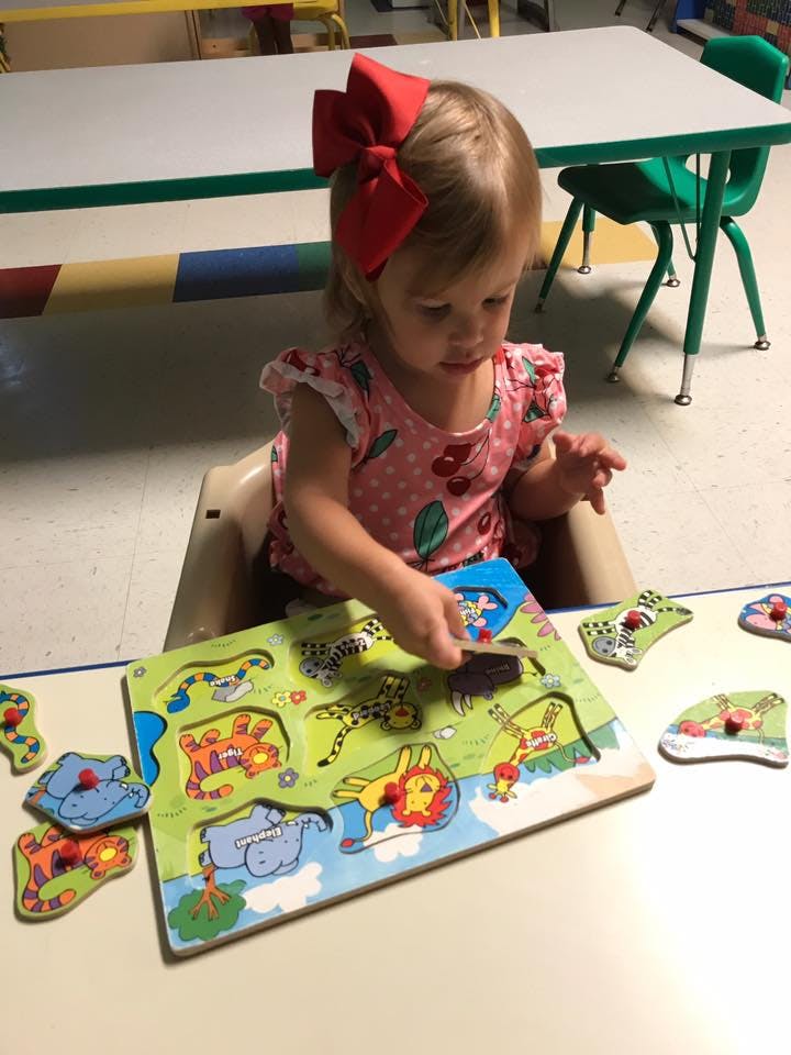 Child playing with a wooden animal puzzle in a classroom