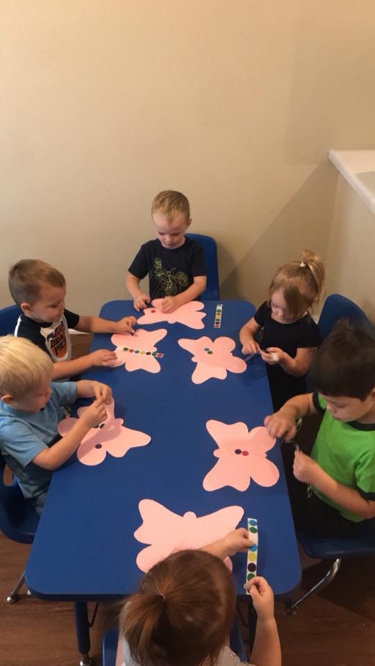 Children at a table decorating butterfly cutouts with small colorful dots
