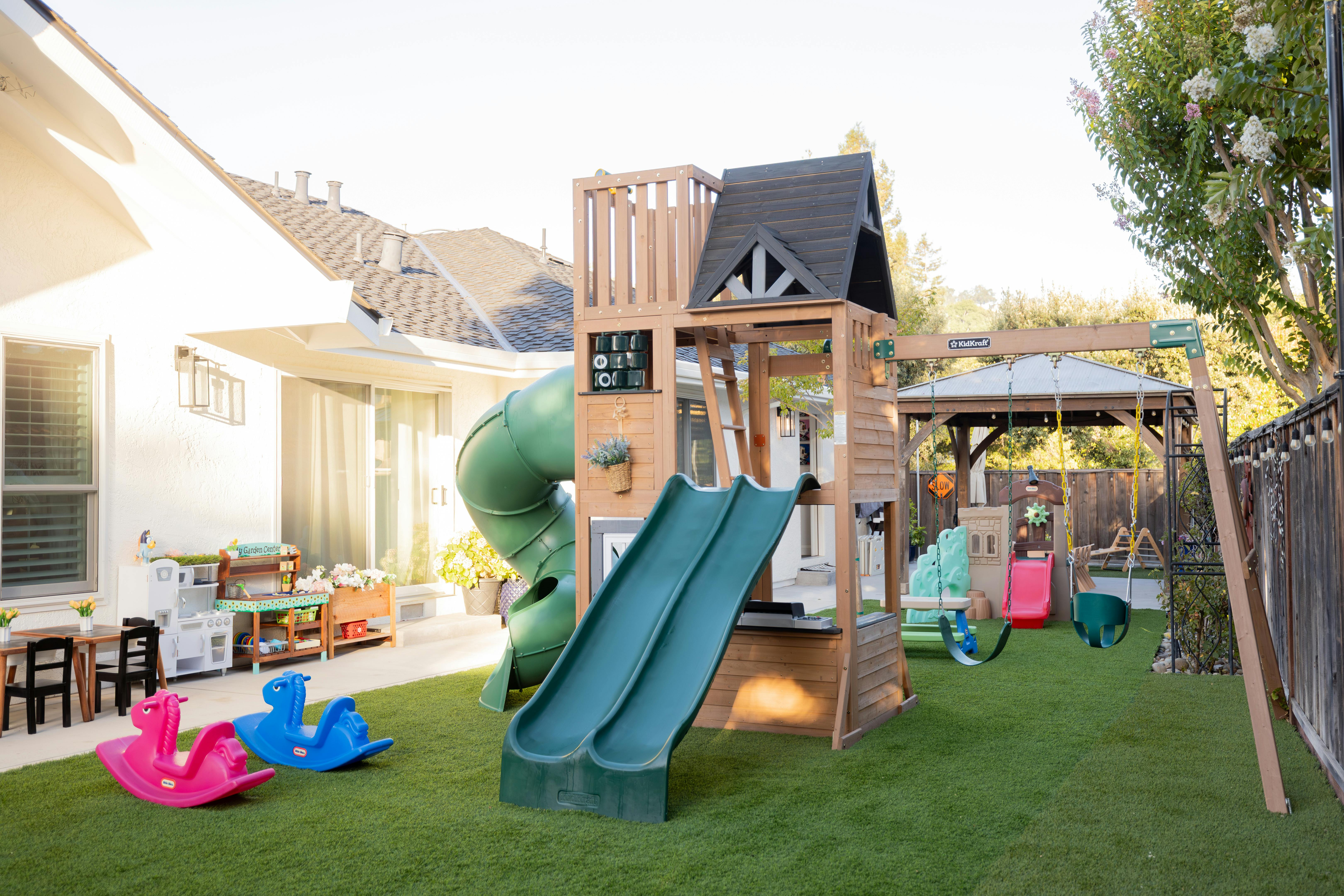Wooden playset with slides and swings in a backyard with artificial grass