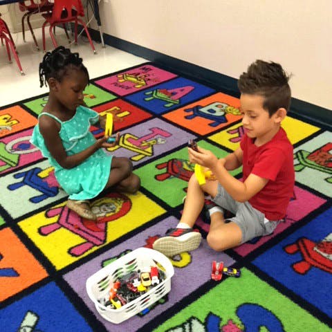 Two children playing with toys on a colorful alphabet rug