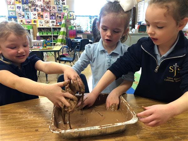 Three children playing with mud in a classroom