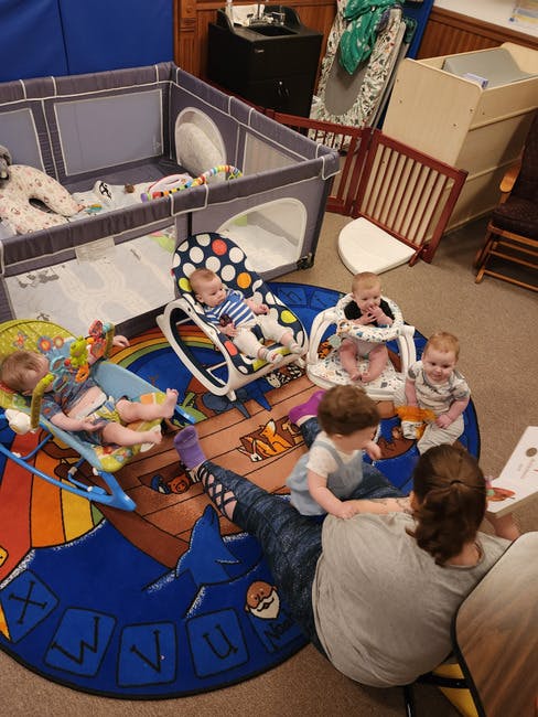 Adult and multiple children and babies on a rug with letters