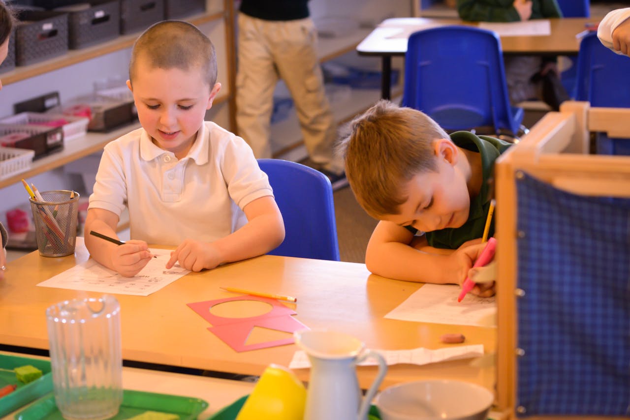 Two children drawing at a table in a classroom