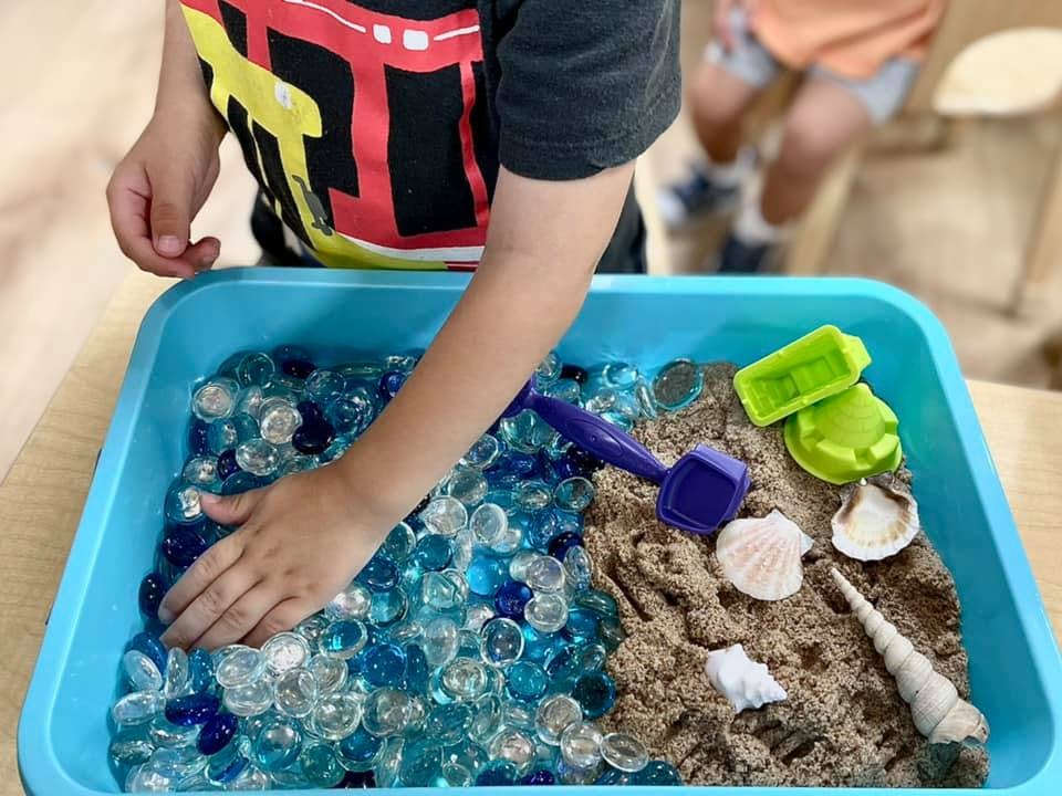 Child playing with water beads and sand in a blue bin