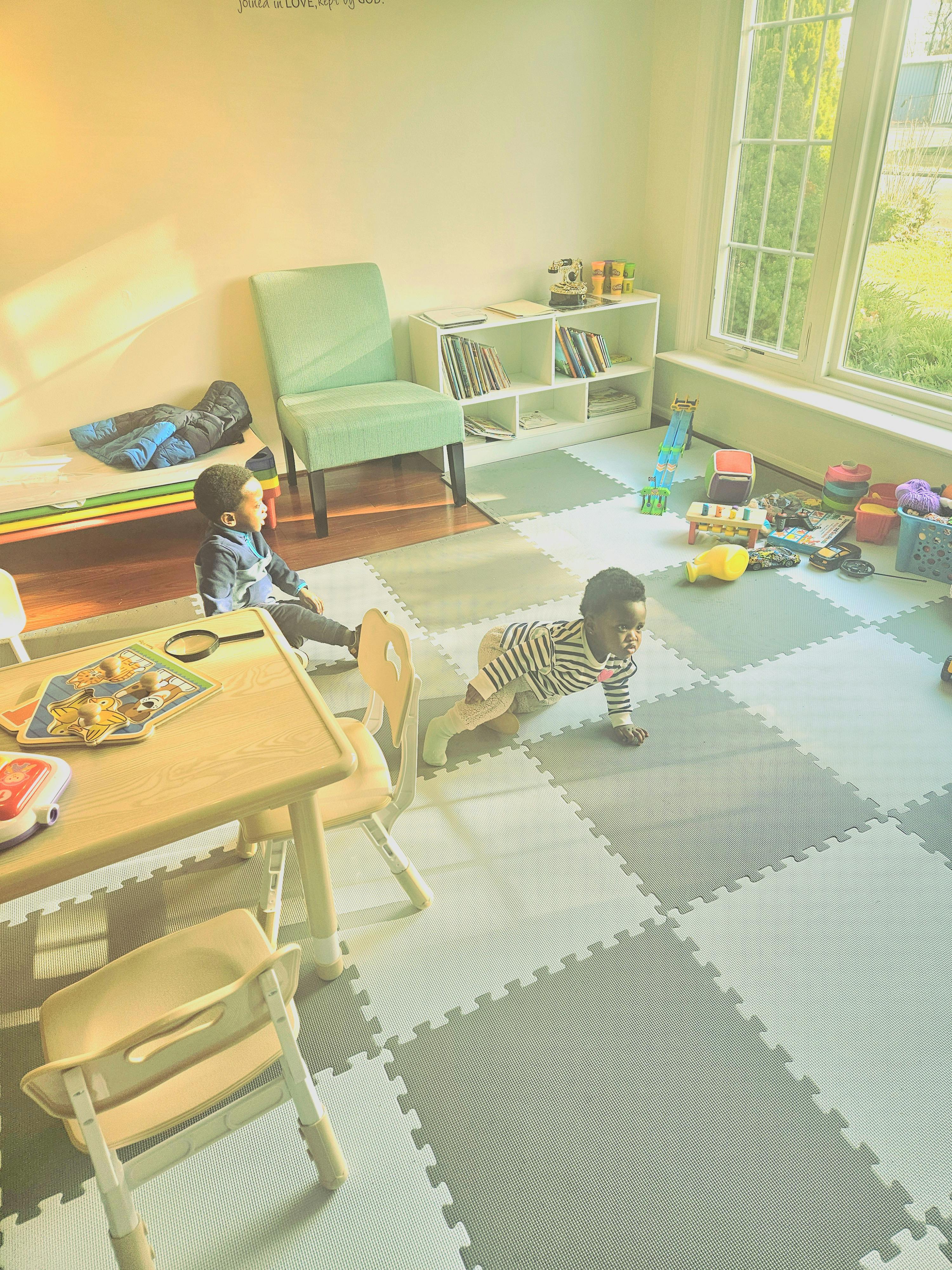 Two children in a playroom, one sitting and one crawling