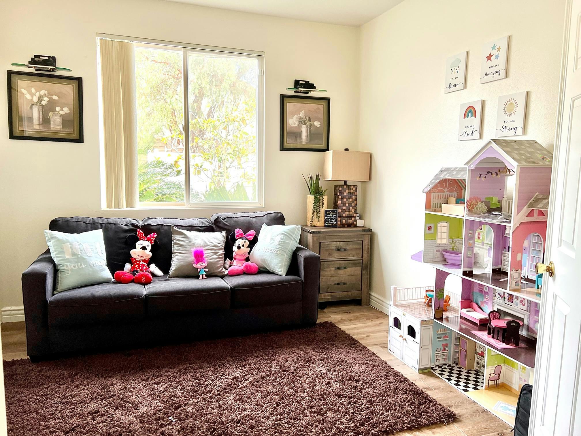 Living room with a dark sofa, brown rug, and a large dollhouse
