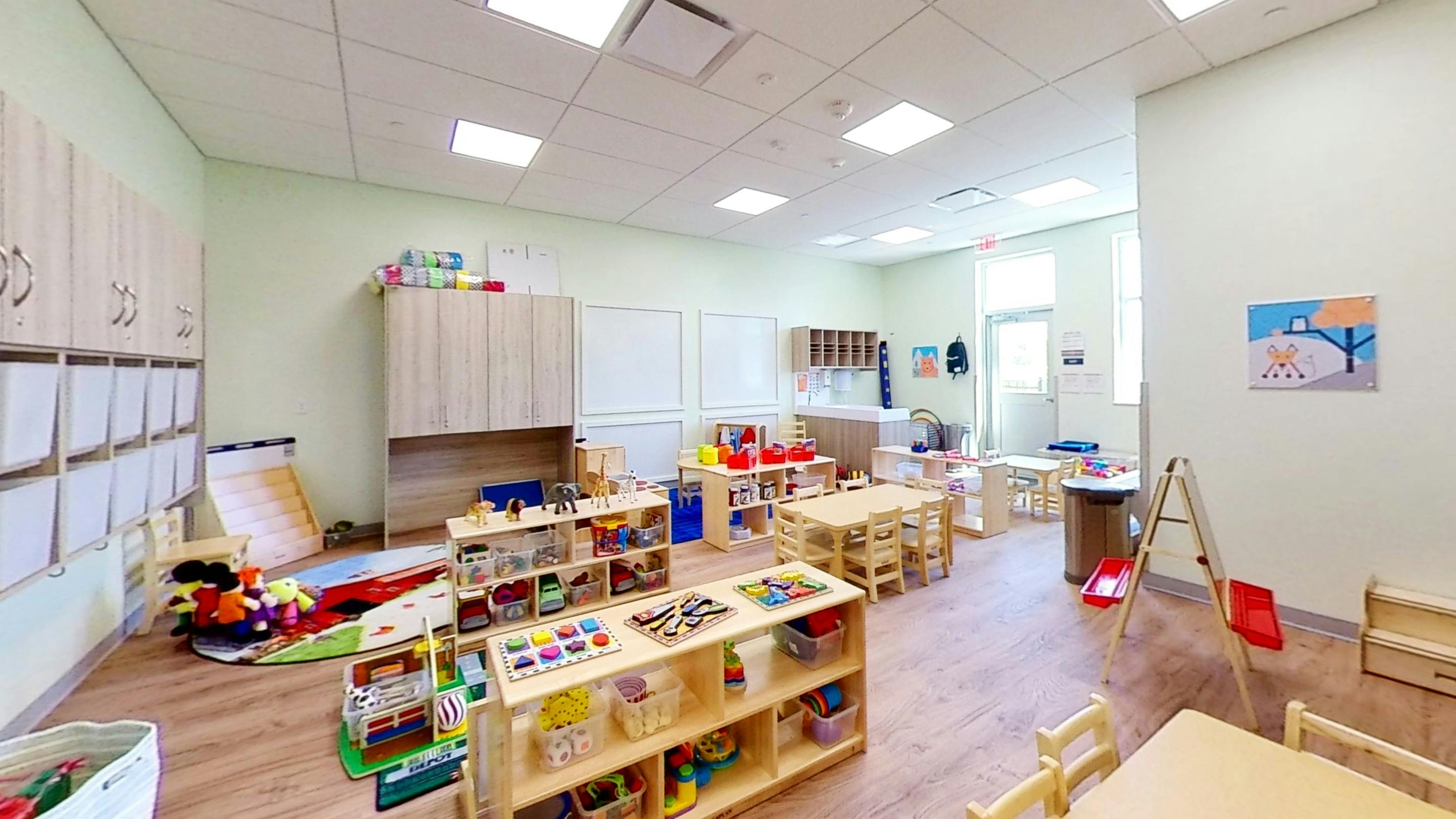 A classroom with small tables and chairs, shelves with toys and learning materials