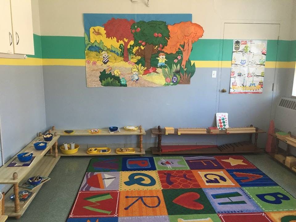 Classroom with alphabet rug, shelves with learning materials, and wall art