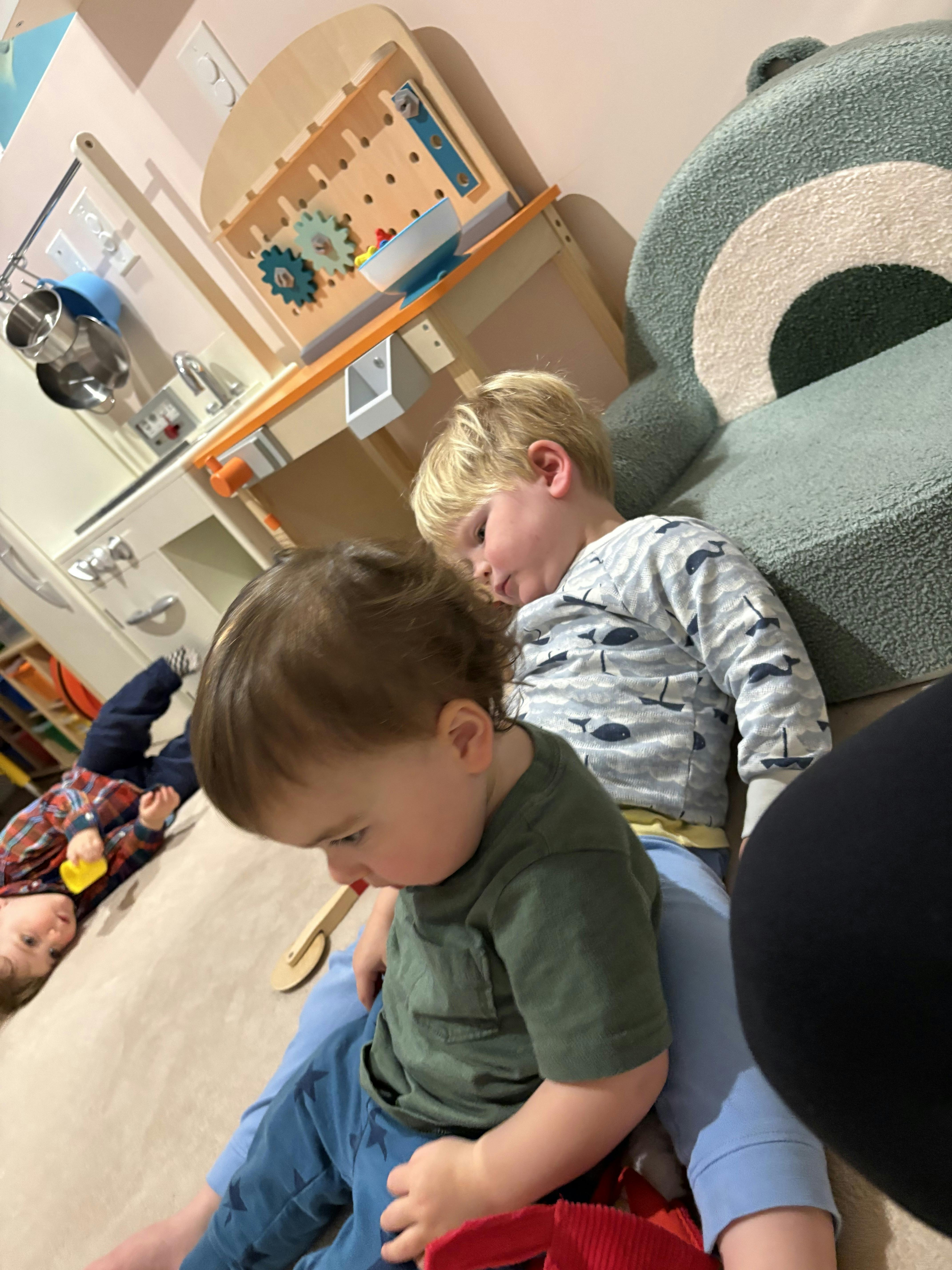 Three children playing on the floor near a toy kitchen and workbench