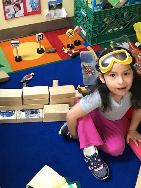 Child wearing goggles sitting on a colorful rug with toy blocks and signs