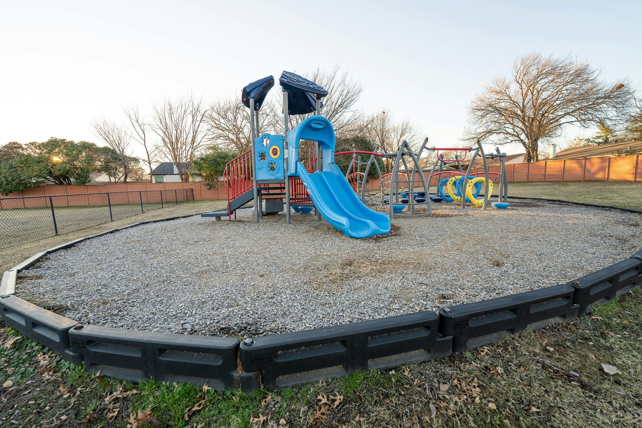 Playground equipment with a slide in a fenced park