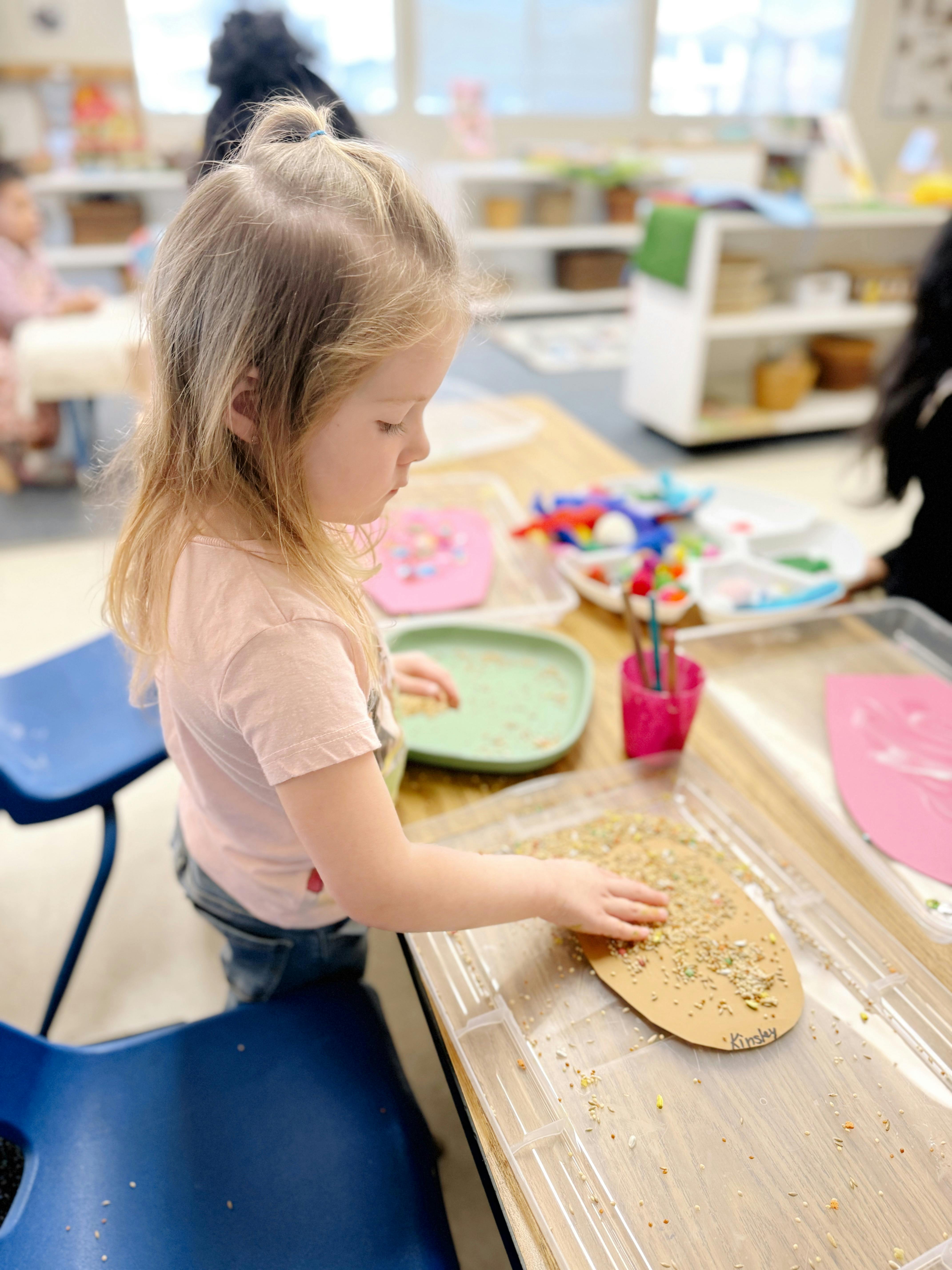 Child playing with craft materials at a table in a classroom