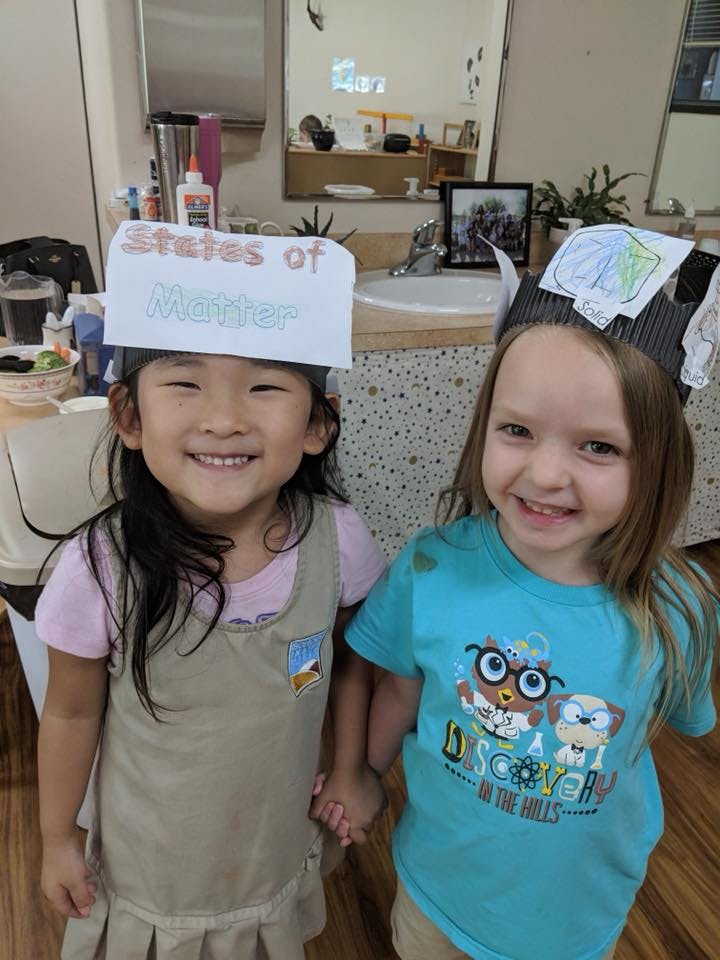 Two children wearing paper hats, holding hands