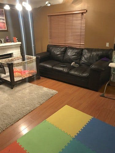 Living room with a black leather couch, baby bassinet, and colorful play mat