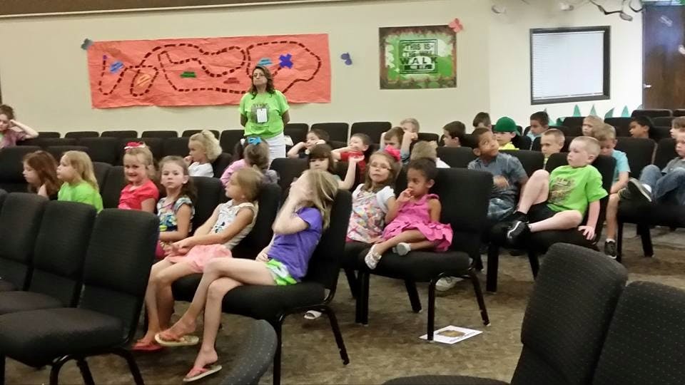 Adult speaking to a group of children seated in rows